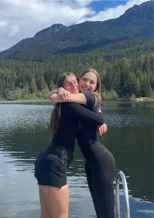 Zwei Mädchen umarmen sich vor einem See und bewaldeten Bergen in Kanada