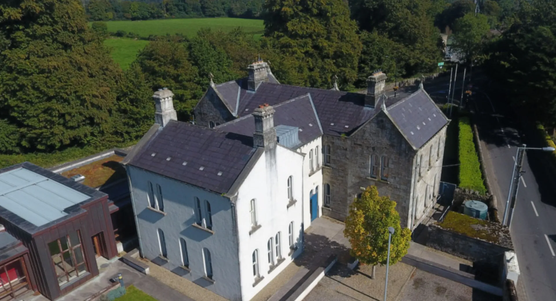 Un edificio residenziale a più piani con tetto in ardesia e camini in un paesaggio alberato all'interno del campus della Blackwater Community School.