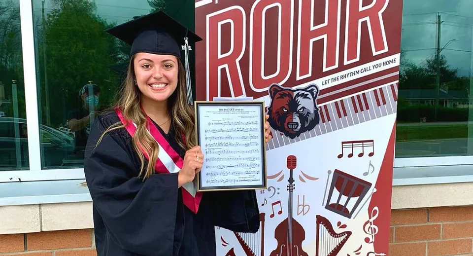Una giovane donna in toga da diploma è in piedi davanti alla grande scritta ROAR alla Georgian Bay District Secondary School.