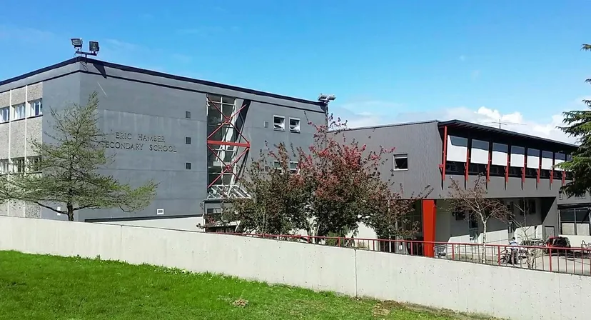 L'edificio moderno a più piani della Eric Hamber Secondary School con facciate in vetro e cemento si trova su un terreno erboso con alberi.