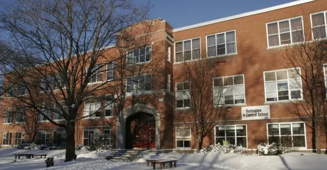 L'edificio in mattoni della Burlington Central High School si trova davanti ad alberi coperti di neve sotto un cielo azzurro e limpido.