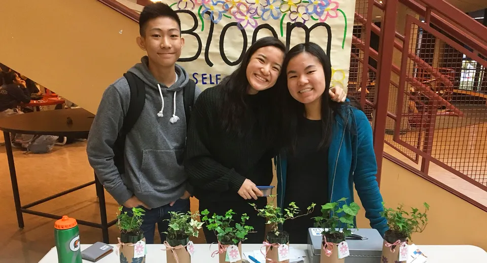 Tre studenti della Magee Secondary School davanti a un murale colorato con la scritta Bloom.