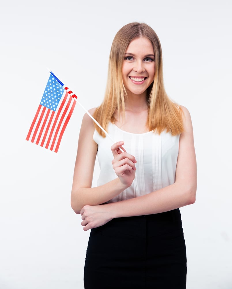 Lächelnde junge Frau hält eine kleine amerikanische Flagge vor weißem Hintergrund