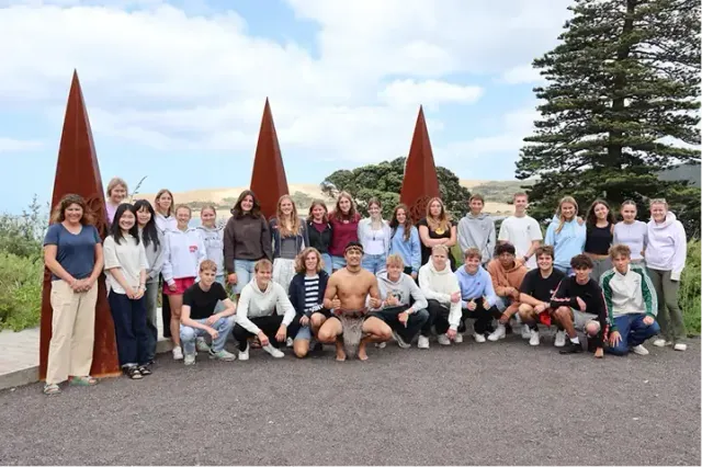Grande gruppo di studenti in posa con sculture maori in legno e un uomo maori in abito tradizionale in Nuova Zelanda