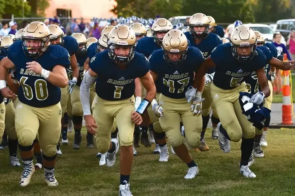 I giocatori di football americano della Hayden Catholic High School corrono sul campo con divise blu e dorate.