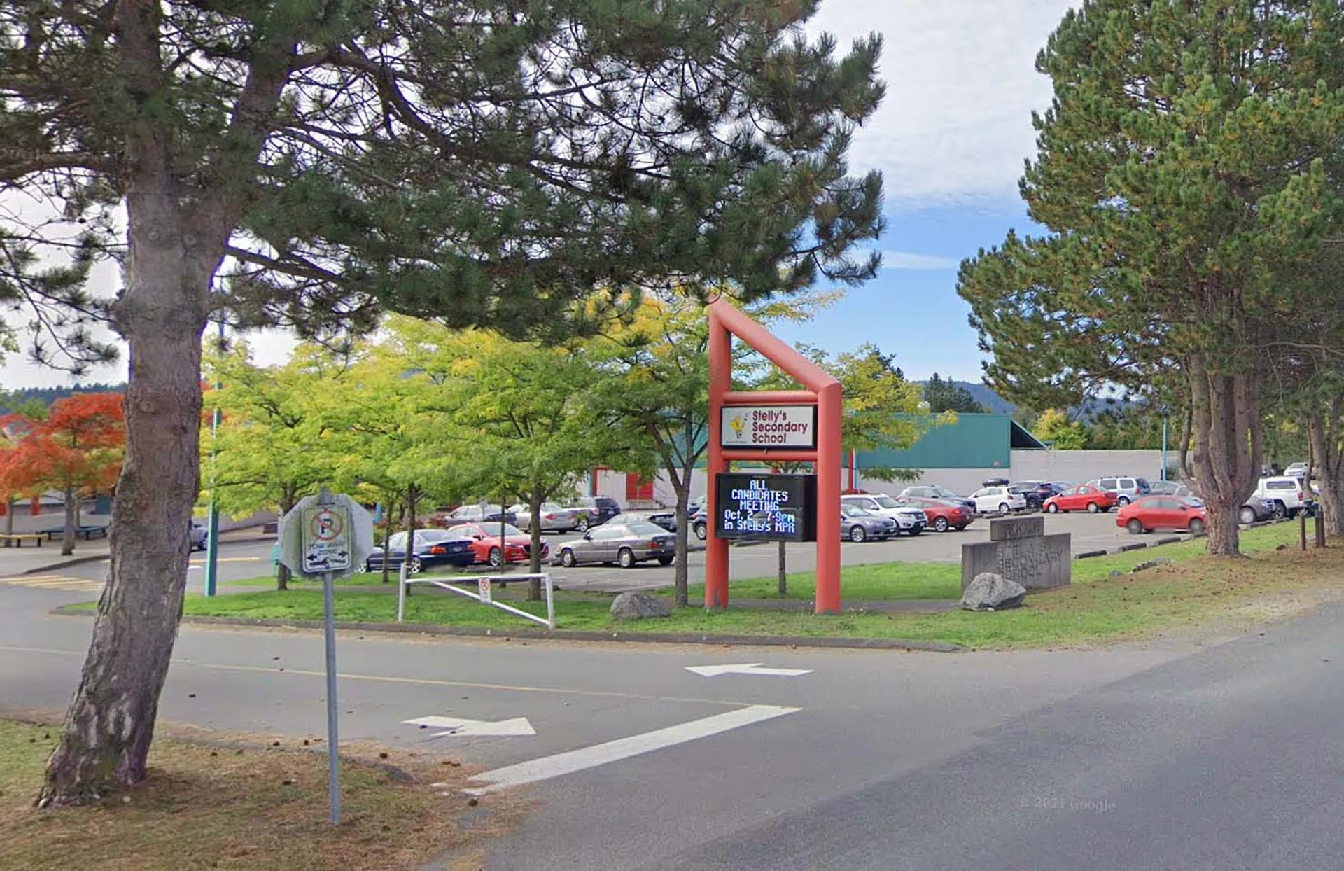 Piccola strada cittadina con negozi, alberi e auto parcheggiate sotto un cielo limpido, vicino alla Stellys Secondary School.