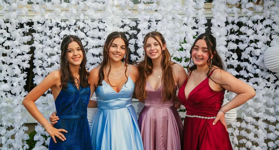 Quattro studentesse della Geraldine High School posano insieme davanti a una decorazione floreale.