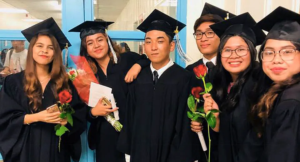 Un gruppo di diplomati in abito da cerimonia posa con dei fiori nel campus del John Polanyi Collegiate Institute.