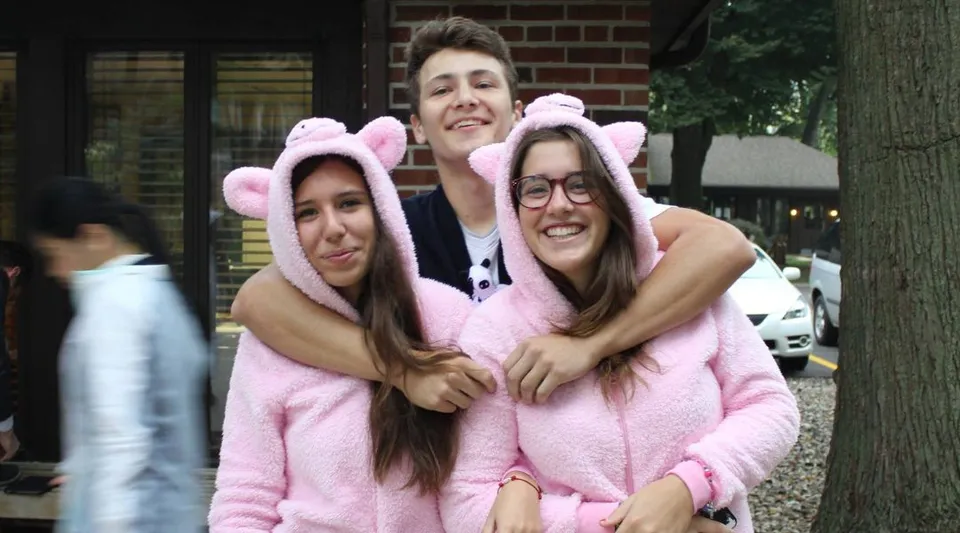 Tre studentesse della La Lumiere School si abbracciano sorridendo davanti a un edificio in mattoni.