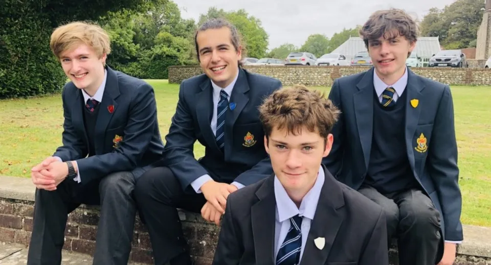 Quattro studenti in divisa scolastica siedono su una panchina all'aperto nel campus del Slindon College.