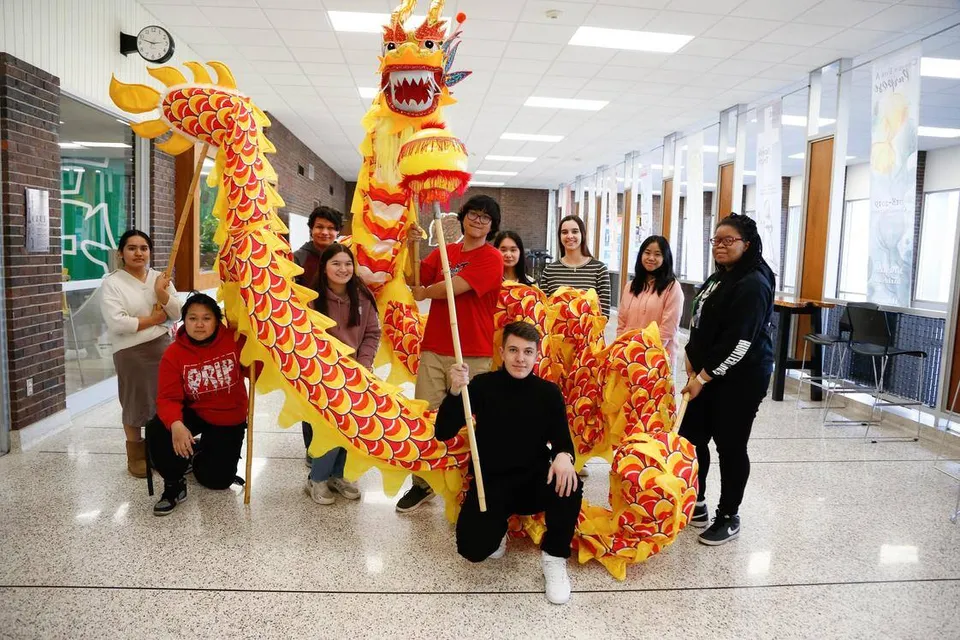 Un gruppo di studenti in abiti tradizionali cinesi con un grande costume da danza del drago nel corridoio della Martin Luther High School.