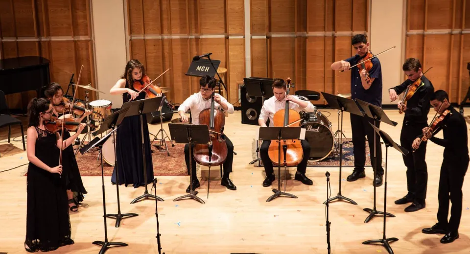 Studenti della Somervale School suonano vari strumenti durante un concerto in una sala da concerto in legno.