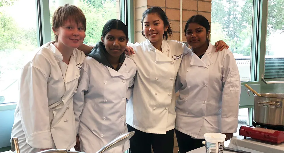 Quattro studenti della Garibaldi Secondary School sono insieme nella cucina della scuola in divisa da cuoco.