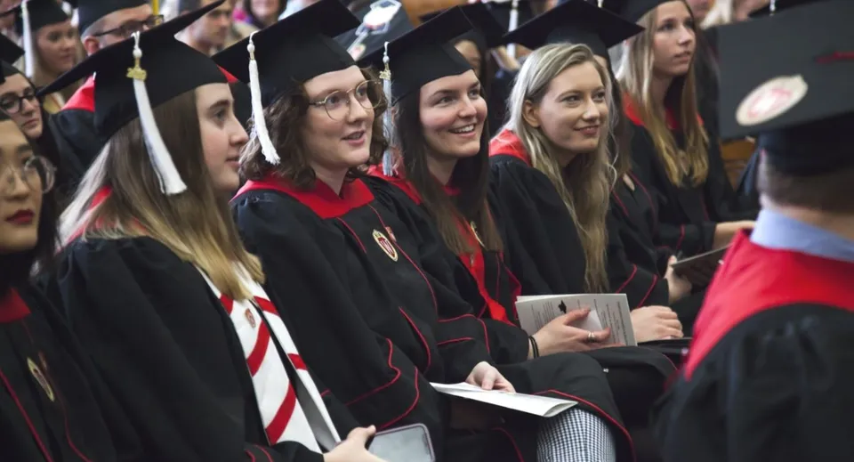 Un gruppo di diplomati della Listowel District Secondary School in toga nera e rossa mostra con orgoglio i propri diplomi.