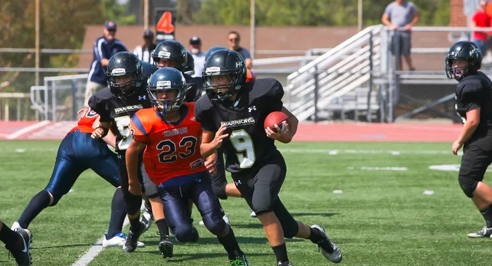 Studenti della Heritage Christian School giocano a calcio sul campo sportivo con spettatori sullo sfondo.