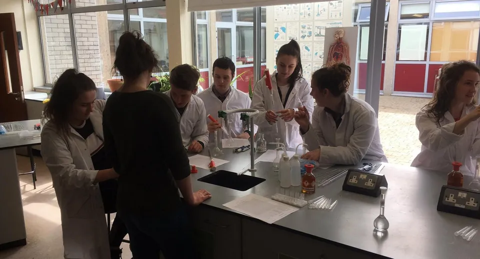 Studenti del Dungarvan College in camice bianco da laboratorio intorno a un tavolo in laboratorio.