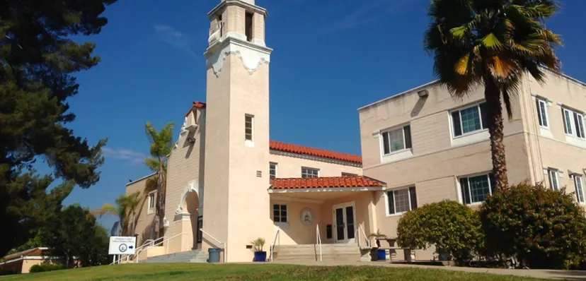 L'edificio di Christian Unified Schools con una torre, tegole rosse e una palma davanti a un cielo azzurro.