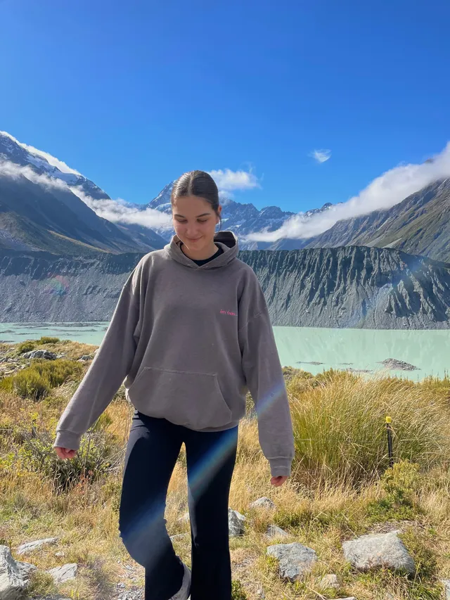 Chica paseando por un sendero de montaña con un lago glaciar y cumbres nevadas al fondo