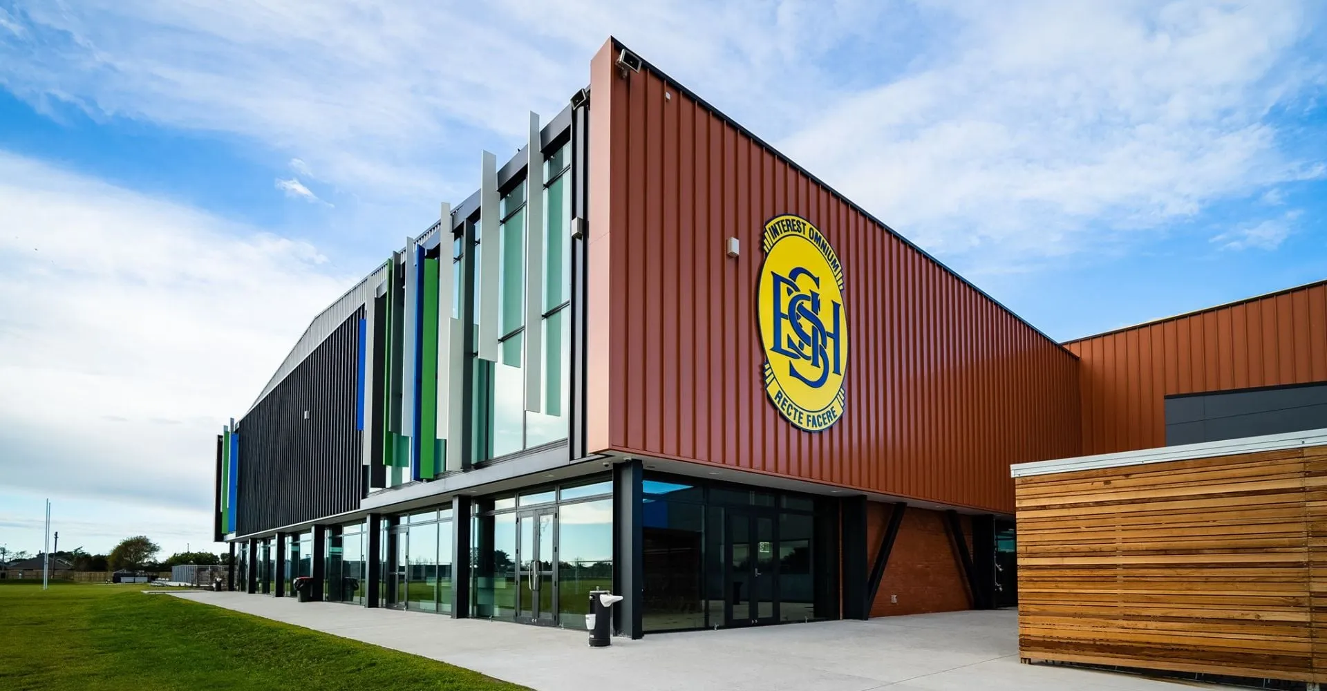 L'edificio multicolore con il grande logo giallo della Shirley Boys' High School si trova su un terreno erboso sotto un cielo blu.