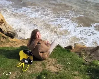 Chica sentada en un acantilado cubierto de hierba sobre las olas del mar