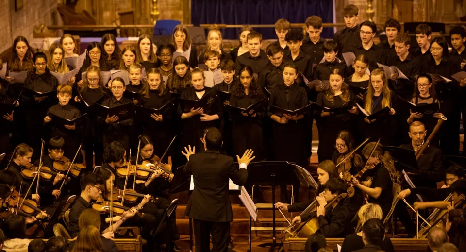 Un grande coro in toghe nere canta sul palco davanti a un'orchestra alla Caterham School.