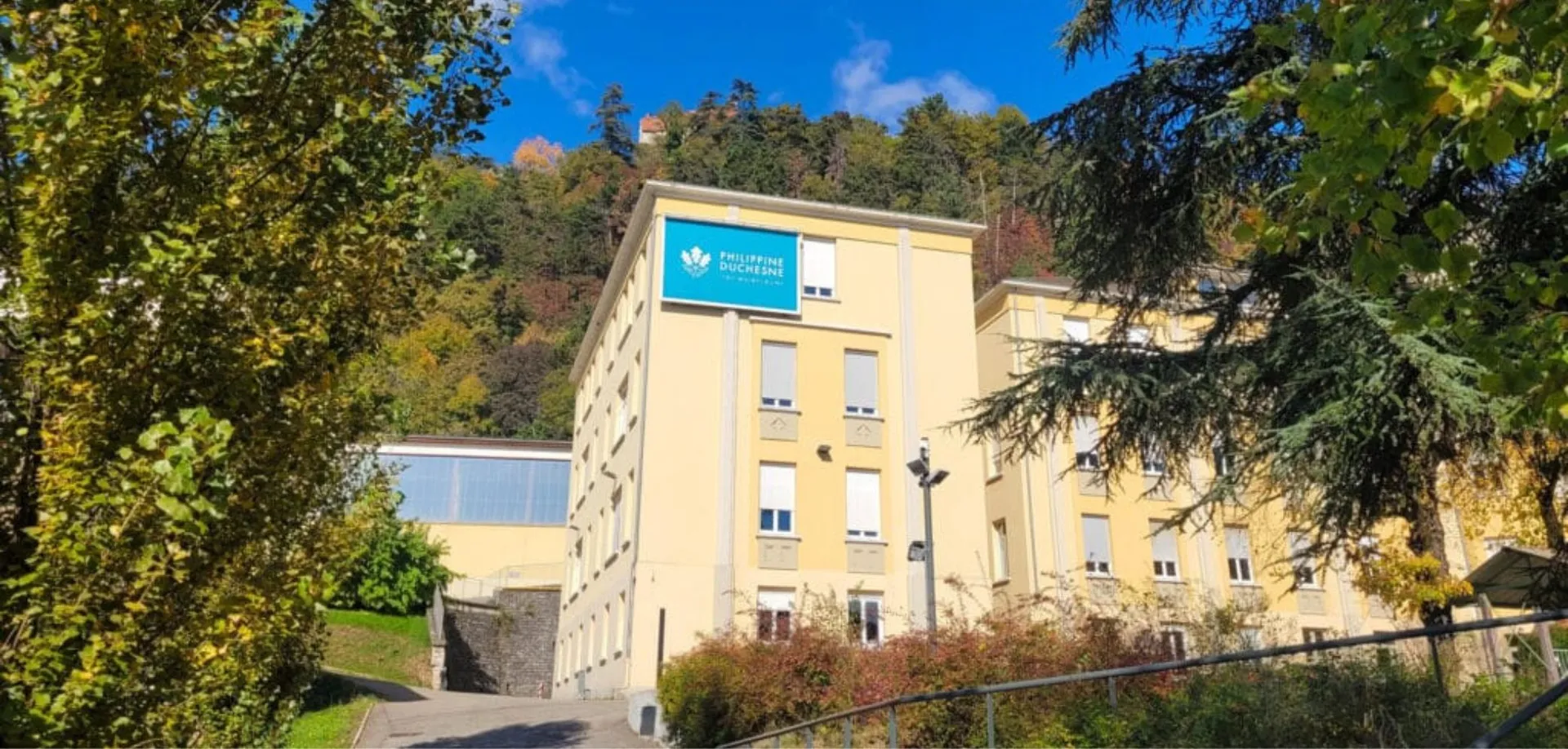 L'edificio giallo a più piani con il logo della Western Norway University of Applied Sciences si trova nel campus del Lycée Polyvalent Philippine Duschenes, circondato da alberi.