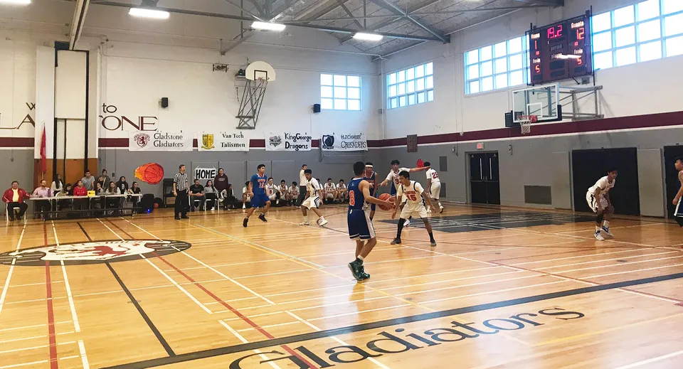Studenti della Gladstone Secondary School giocano attivamente una partita di basket in una palestra luminosa con grandi finestre.