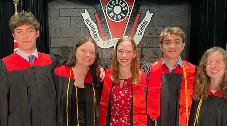 Cinque studenti e studentesse della Glengarry District High School indossano l'abito da diploma davanti a uno stemma universitario.