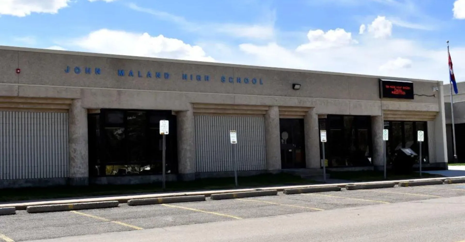 L'ampio edificio scolastico grigio della John Mallard High School è chiaramente riconoscibile con il suo nome sulla facciata.