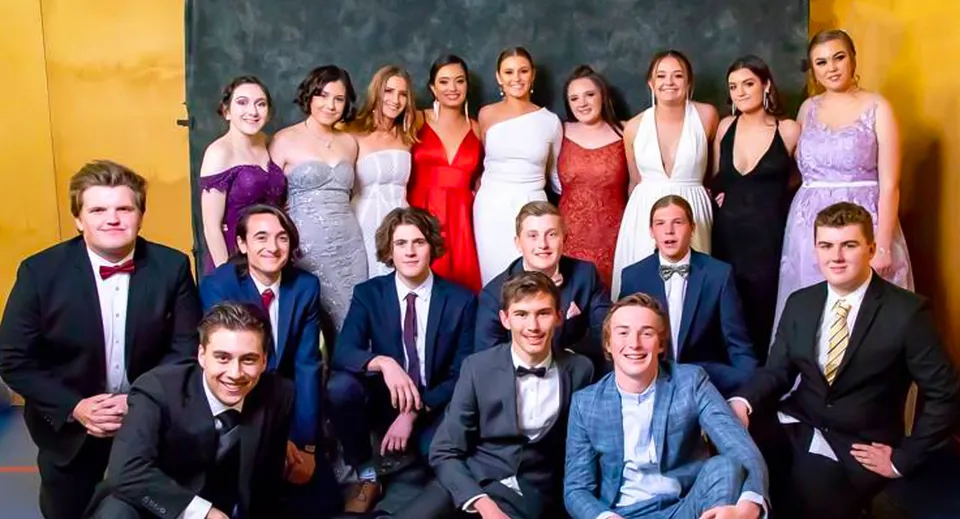 Un gruppo di studenti in abito formale posa davanti a uno sfondo giallo nel campus della Roxby Downs Area School.