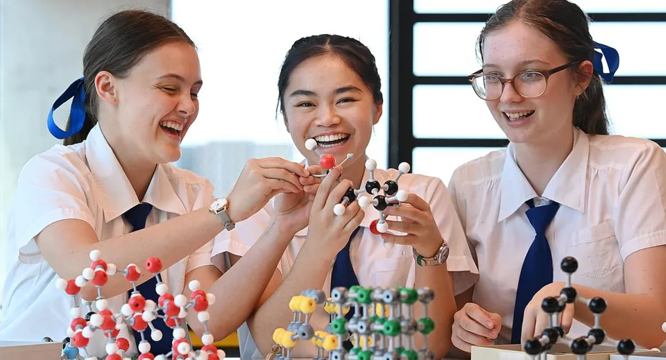 Tre studentesse della Ardscoil Mhuire esaminano sorridenti modelli molecolari colorati in un laboratorio.