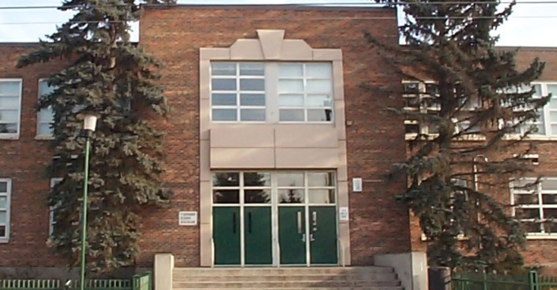 L'ingresso dell'edificio in mattoni della Queen Elizabeth School con due grandi pini ai lati.