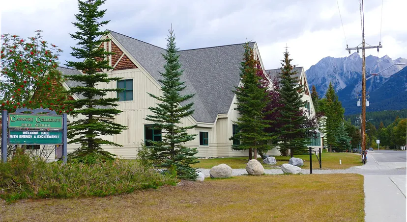 L'edificio rustico della Canmore Collegiate High School sorge immerso in un paesaggio boschivo con pini alti e montagne sullo sfondo.