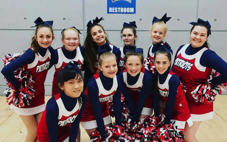 Un gruppo di cheerleader in uniformi coordinate posa davanti a un cartello dei bagni nel campus della American Heritage Academy.