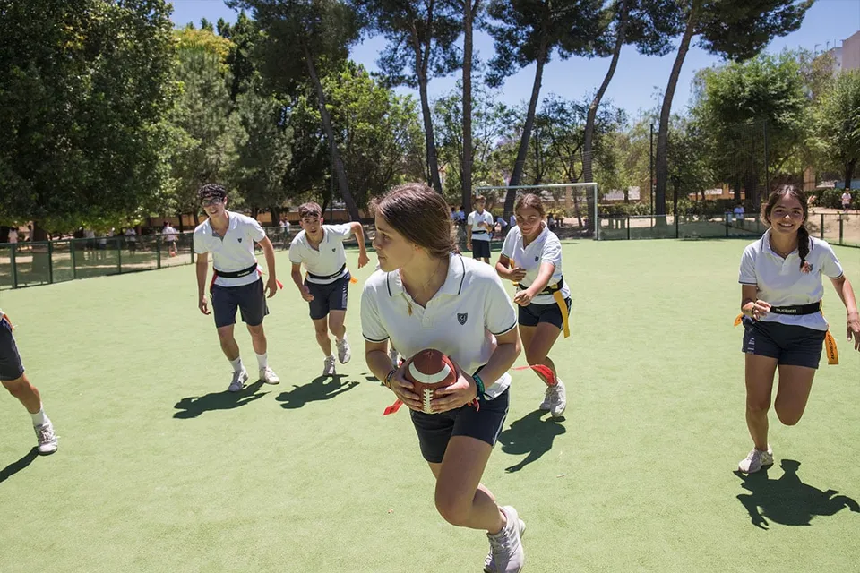 Un gruppo di studenti in divisa sportiva si trova sul campo sportivo della Yago School con alberi ed edifici sullo sfondo.