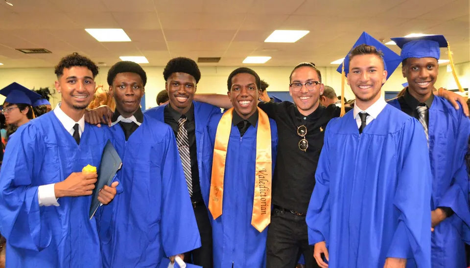 Un gruppo di diplomati in posa con toghe blu e tocchi nel campus del West Humber Collegiate Institute.