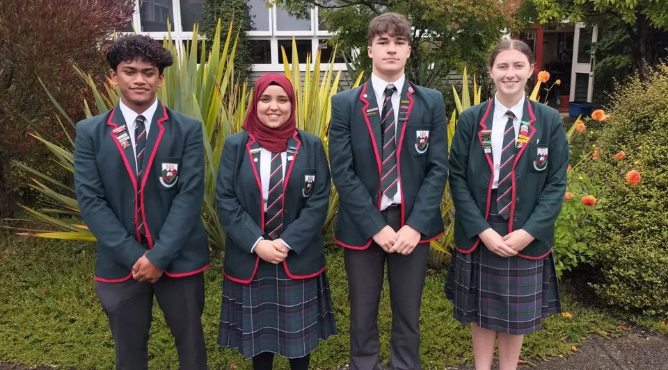 Un gruppo di studenti del Kaikorai Valley College si trova davanti a un edificio con molto verde sullo sfondo.