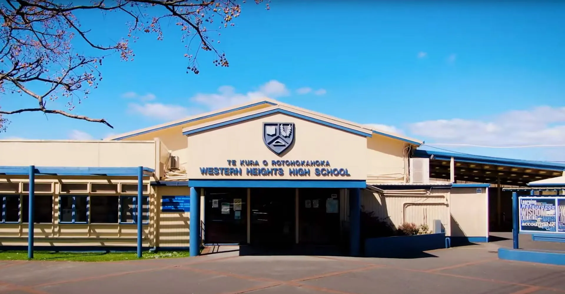 L'edificio della Western Heights High School si trova sotto un cielo blu con alberi in fiore sullo sfondo.