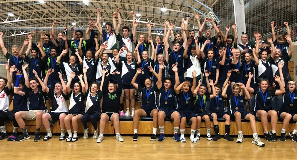 Un gruppo di studenti della Craigslea State High School posa insieme nella palestra con le braccia alzate.