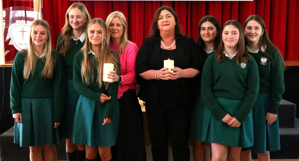 Studentesse della Holy Child Secondary School posano con due donne e candele accese davanti a una tenda rossa.