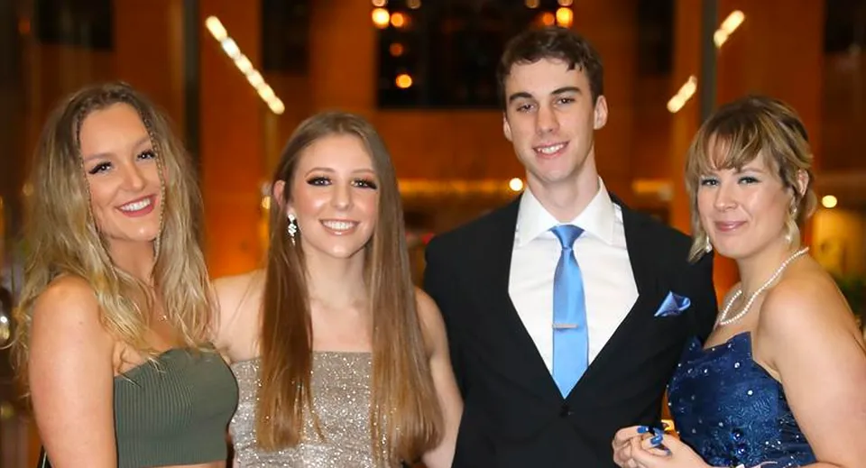 Quattro persone, due donne e due uomini, posano insieme davanti a uno sfondo decorativo nel campus della Australian Science and Mathematics School.