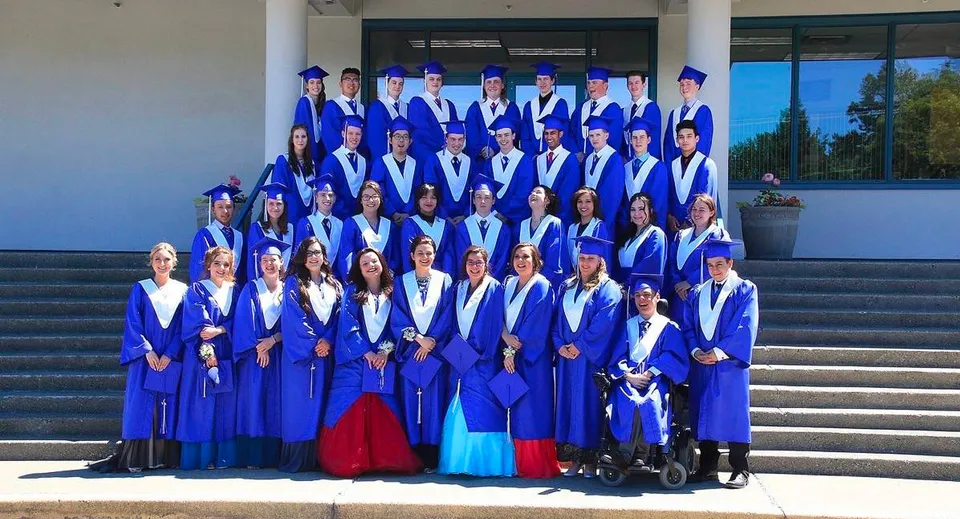 Diplomati della Lake Cowichan Secondary School in toga blu posano sulle scale davanti all'edificio scolastico.