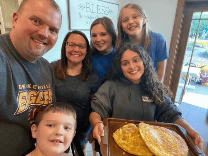 Una joven muestra una bandeja con dos tortillas frente a su familia sonriente en casa