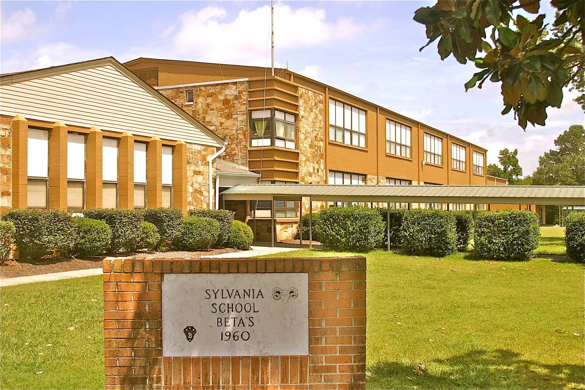 L'edificio a due piani della Sylvania High School, con rivestimento in mattoni e pannelli laterali, è circondato da un prato curato e cespugli.