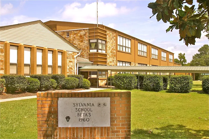 L'edificio a due piani della Sylvania High School, con rivestimento in mattoni e pannelli laterali, è circondato da un prato curato e cespugli.
