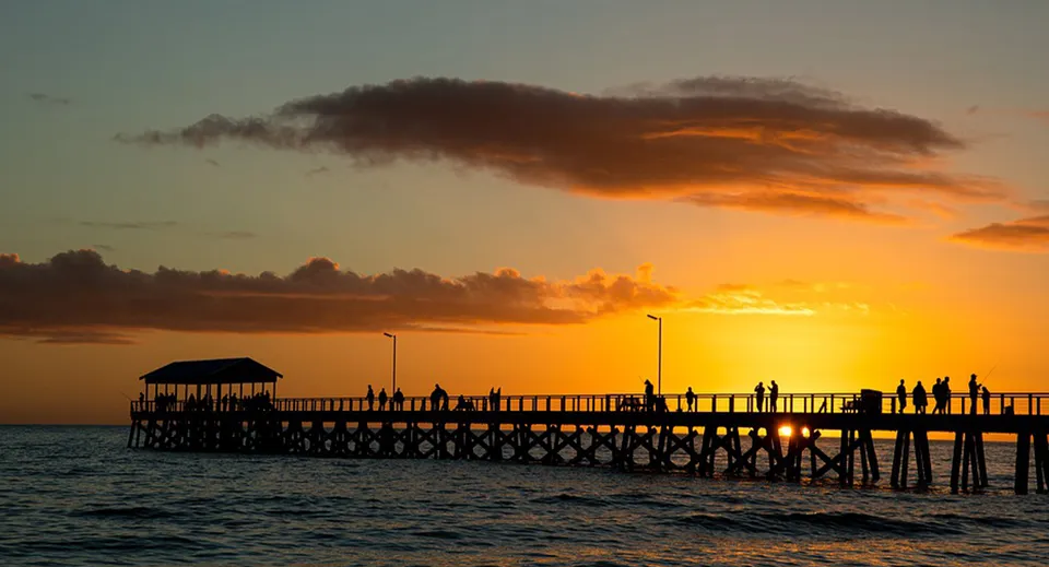 Un pontile in legno si estende sull'acqua al tramonto con nuvole suggestive all'interno della Coolum State High School.