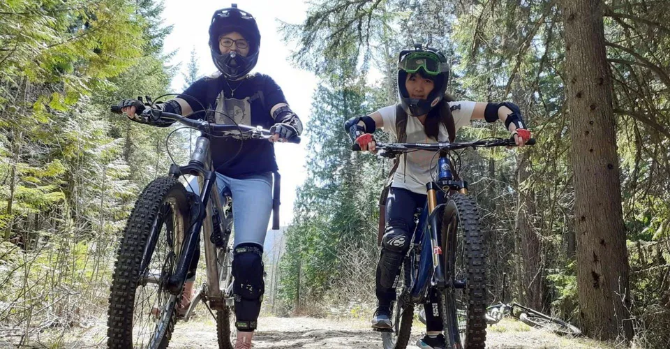 Due persone del Waterloo Region District School Board vanno in mountain bike su un sentiero nel bosco indossando un abbigliamento protettivo.