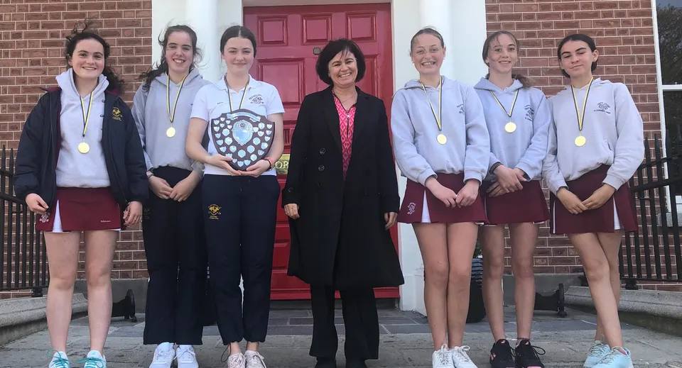 Sei studentesse del Loreto College, St. Stephen's Green posano con medaglie e un trofeo davanti a una porta rossa.