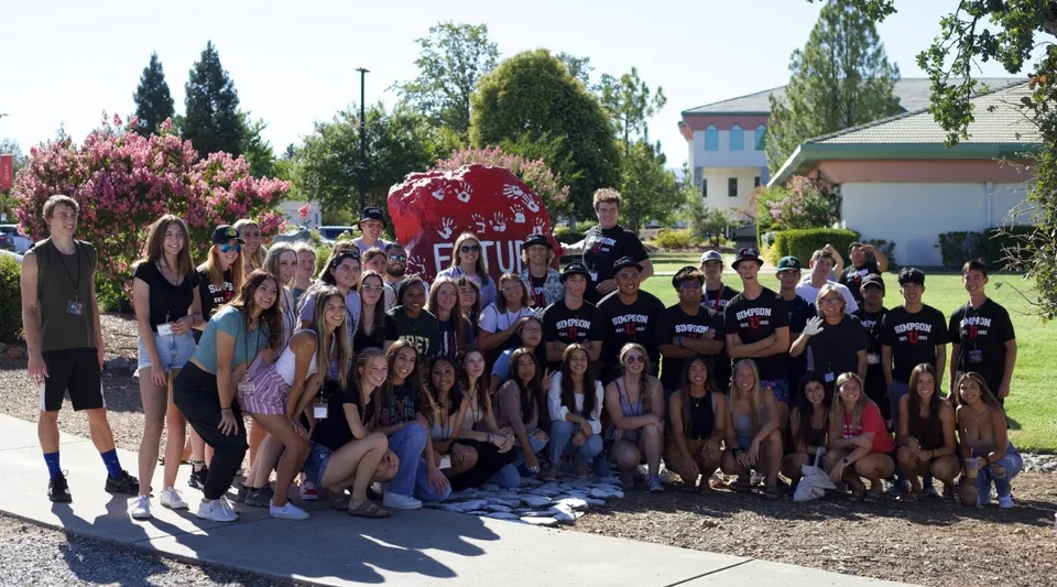 Un grande gruppo di studenti si trova nel parco del campus della Simpson University.