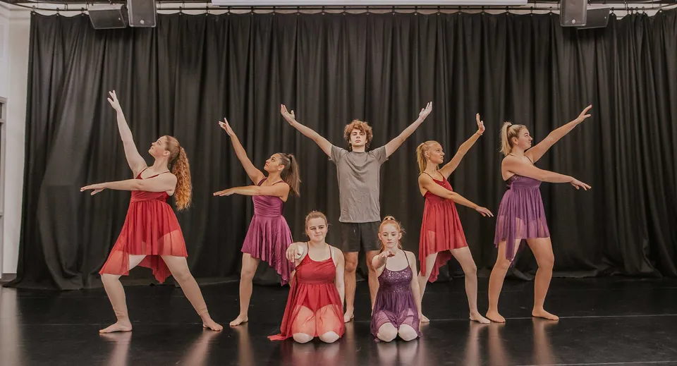 Un gruppo di ballerini e ballerine si esibisce sul palco del Reynella East College in uno spettacolo di danza con costumi colorati.